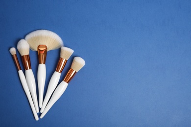 Photo of Flat lay composition with set of professional makeup brushes on blue background. Space for text