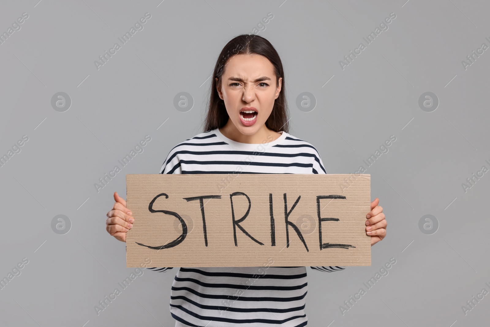 Photo of Angry young woman holding cardboard banner with word Strike on light grey background