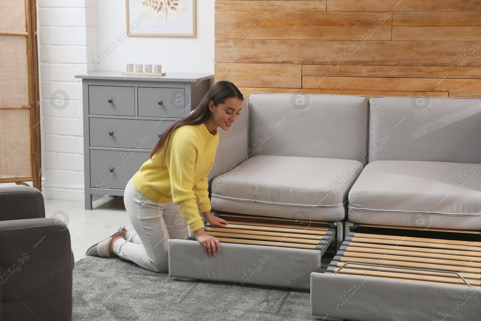 Photo of Young woman unfolding sofa into a bed in room. Modern interior