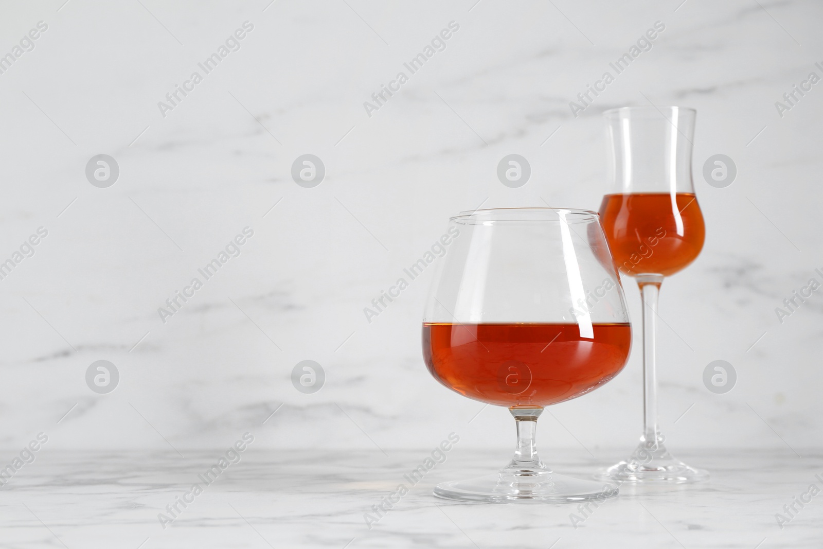 Photo of Delicious liqueurs in glasses on white marble table, space for text