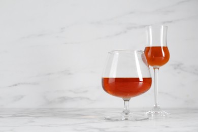 Delicious liqueurs in glasses on white marble table, space for text