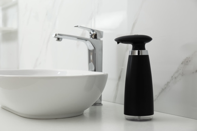 Modern automatic soap dispenser near sink in bathroom, closeup