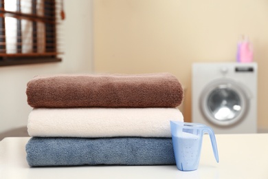 Photo of Clean towels and measuring cup of washing powder on table in laundry room. Space for text