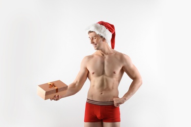 Photo of Young muscular man in Santa hat with gift box on white background