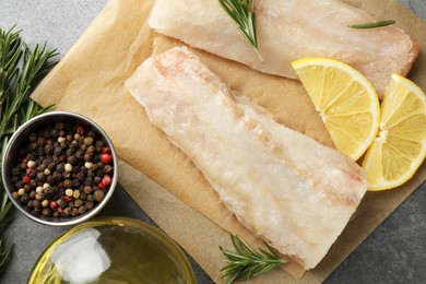 Photo of Fresh raw cod fillets, spices and lemon slices on grey table, flat lay