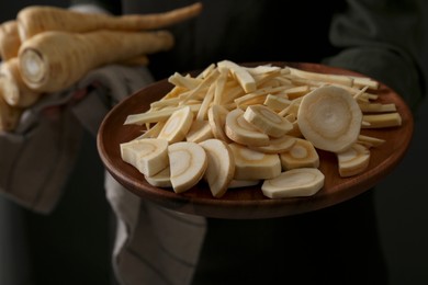 Photo of Woman holding whole and cut parsnips on black background, closeup