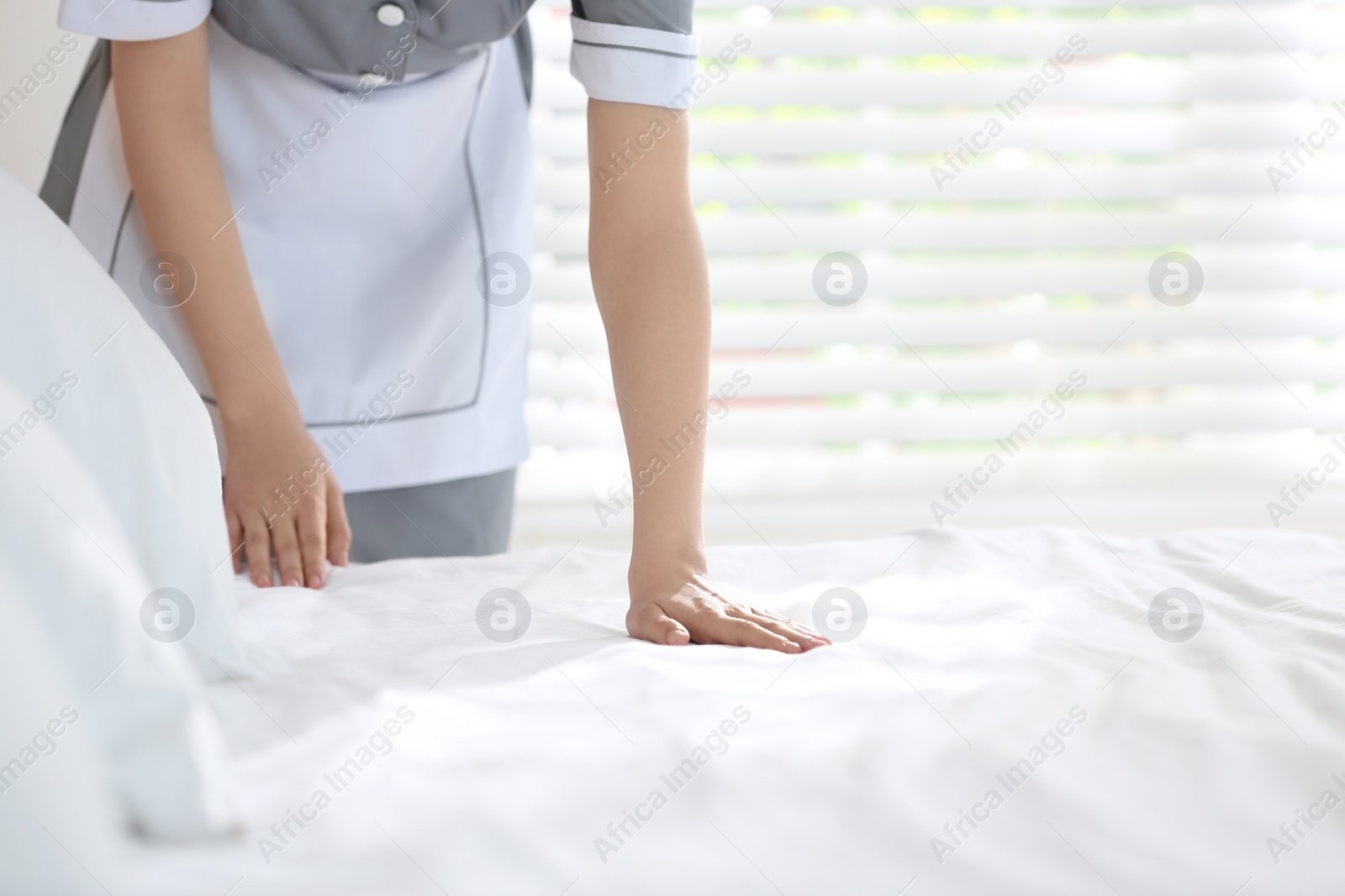 Photo of Young chambermaid making bed in hotel room, closeup