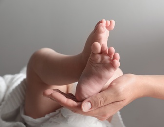 Mother holding her baby on grey background, closeup on feet