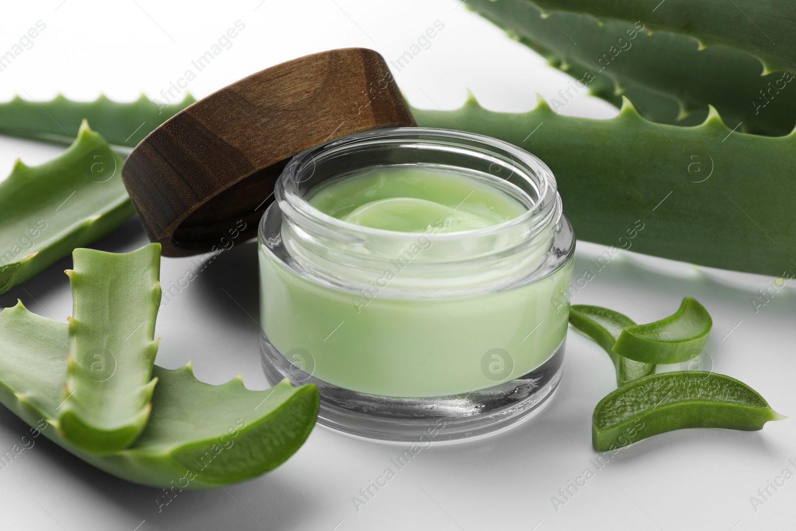 Photo of Jar of natural cream and aloe leaves on white background, closeup