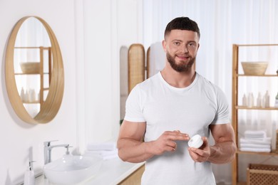 Photo of Handsome man applying body cream in bathroom. Space for text