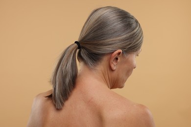 Mature woman with healthy skin on beige background, back view