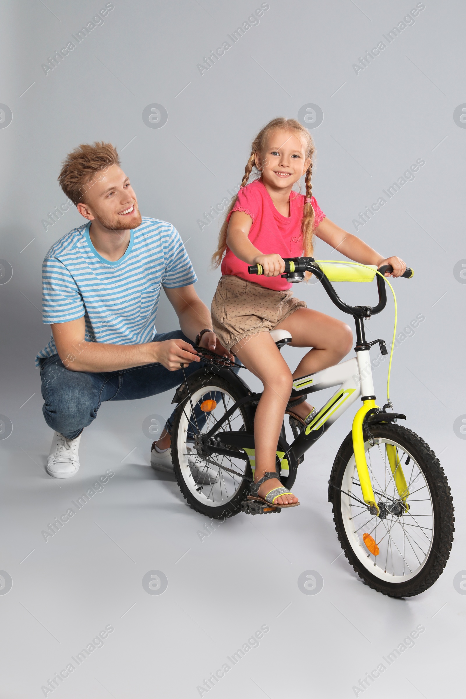 Photo of Young father teaching daughter to ride bicycle on grey background
