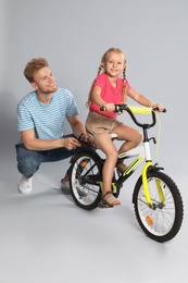 Young father teaching daughter to ride bicycle on grey background