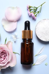 Photo of Bottle of cosmetic serum, beautiful flowers and sea salt on light blue background, flat lay