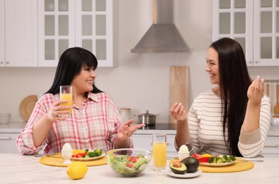 Photo of Happy overweight women having healthy meal together at table in kitchen