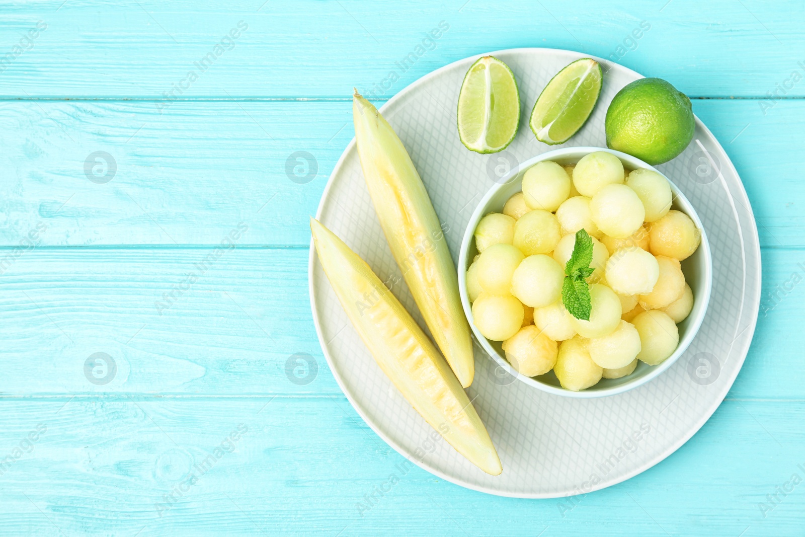 Photo of Melon balls with mint and lime on light blue wooden table, top view. Space for text