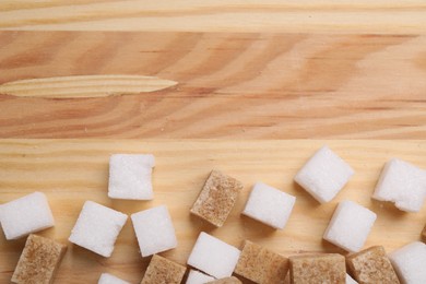 Photo of White and brown sugar cubes on wooden table, flat lay. Space for text