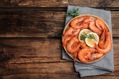 Delicious cooked shrimps with rosemary and lemon on wooden table, top view. Space for text