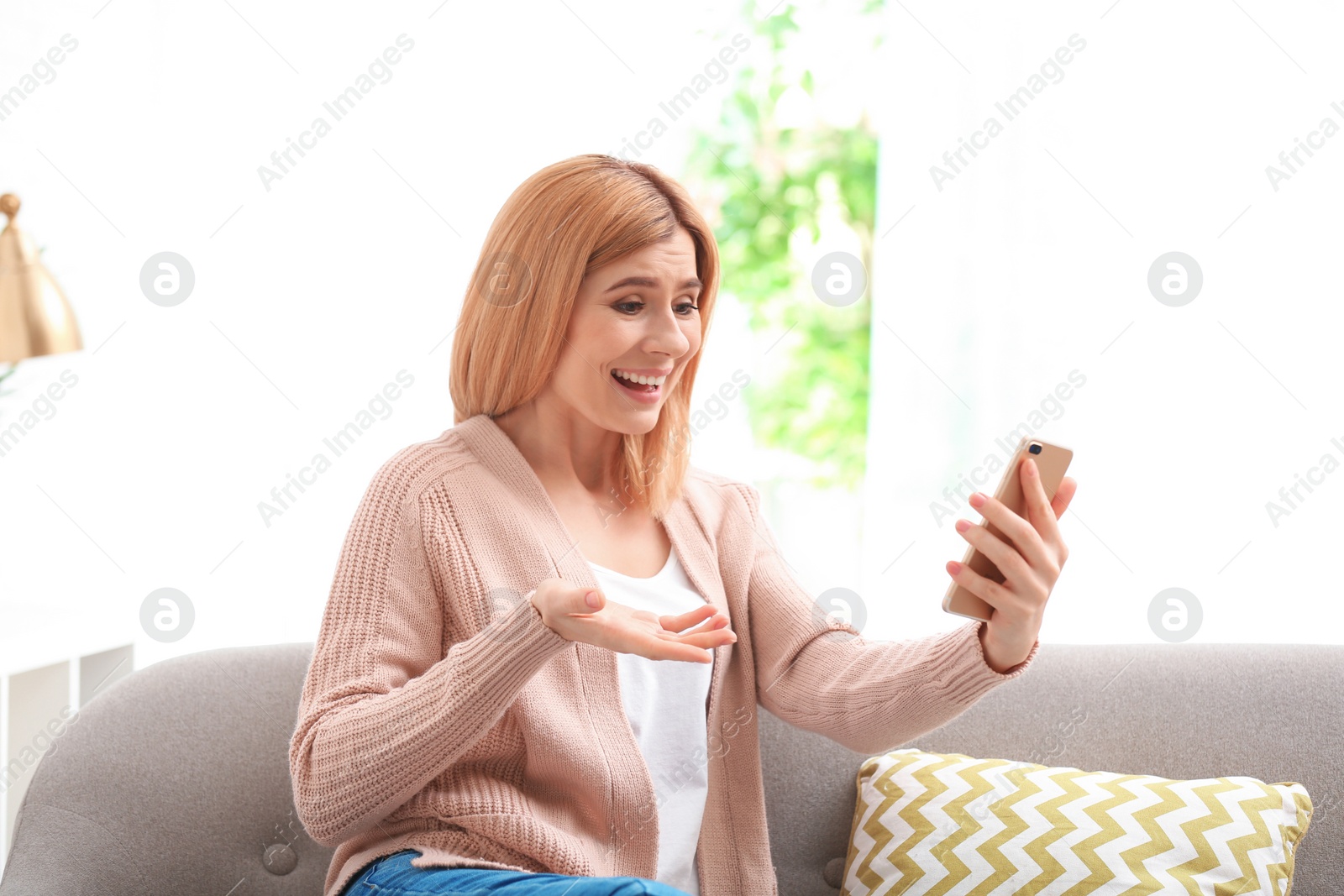 Photo of Woman using mobile phone for video chat in living room