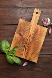 Photo of Cutting board, basil and garlic on wooden table, flat lay. Space for text