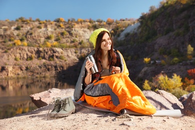 Photo of Female camper with thermos in sleeping bag outdoors