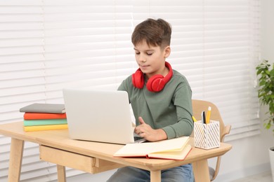 Boy with red headphones using laptop at desk in room. Home workplace