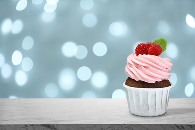 Image of Sweet birthday cupcake with fresh raspberries on marble table against blurred lights. Space for text