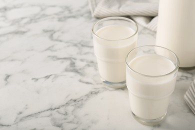 Glasses of fresh milk on white marble table, space for text