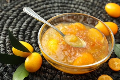 Photo of Delicious kumquat jam and fresh fruits on wicker mat, closeup