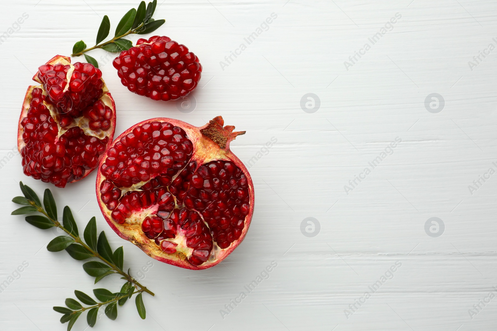 Photo of Pieces of fresh pomegranate and branches on white wooden table, flat lay. Space for text