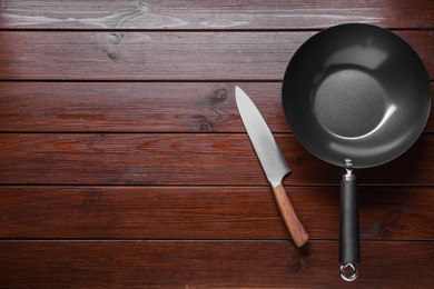 Empty iron wok and knife on wooden table, flat lay. Space for text