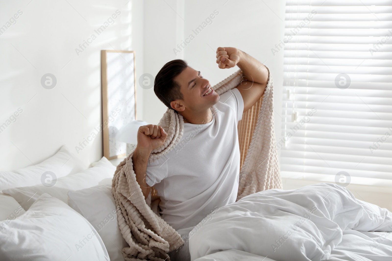 Photo of Man with beige plaid stretching on bed indoors