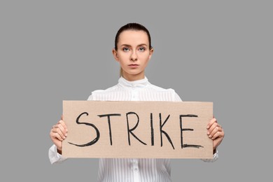 Photo of Woman holding cardboard banner with word Strike on grey background