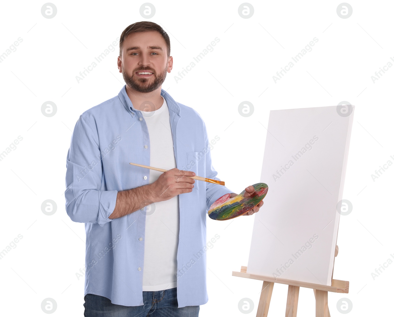 Photo of Man with painting tools near easel on white background. Young artist
