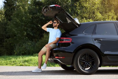 Happy man sitting in trunk of modern car outdoors