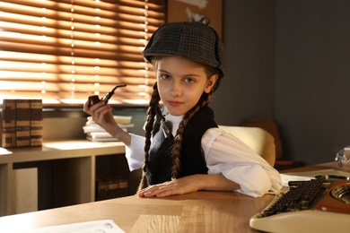 Photo of Cute little detective with smoking pipe at table in office
