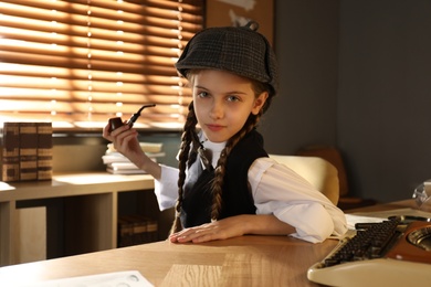 Cute little detective with smoking pipe at table in office