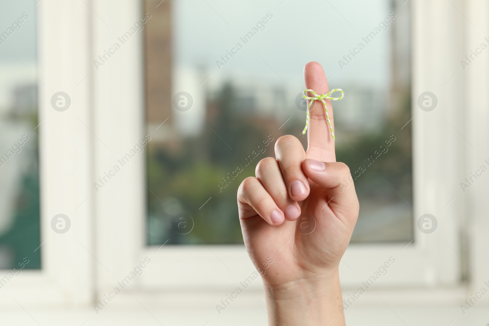 Photo of Man showing index finger with tied bow as reminder near windows indoors, closeup. Space for text