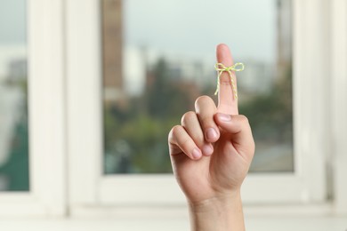 Photo of Man showing index finger with tied bow as reminder near windows indoors, closeup. Space for text