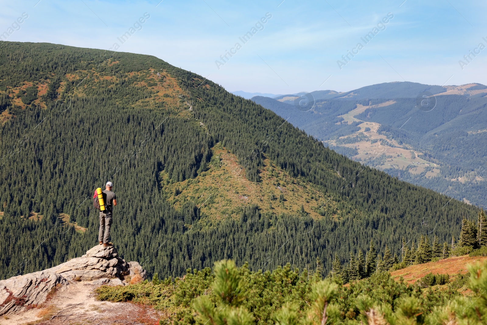 Photo of Man with backpack on rocky peak in mountains, back view