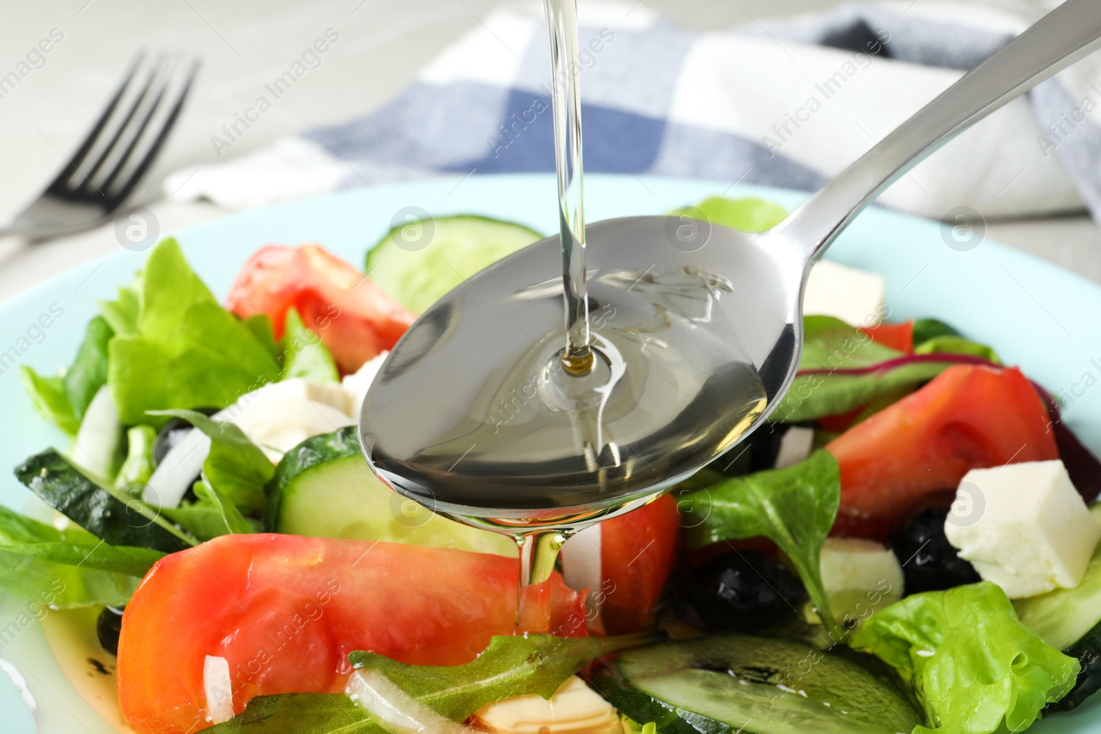 Photo of Adding cooking oil to delicious salad on table, closeup