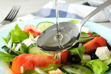 Adding cooking oil to delicious salad on table, closeup