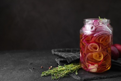 Jar with tasty pickled onions on black table, space for text