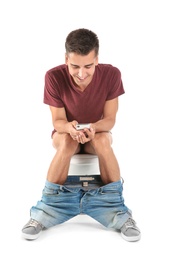 Photo of Young man using mobile phone while sitting on toilet bowl. Isolated on white