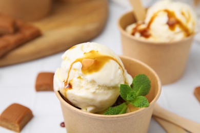 Photo of Scoopsice cream with caramel sauce, mint leaves and candies on white table, closeup