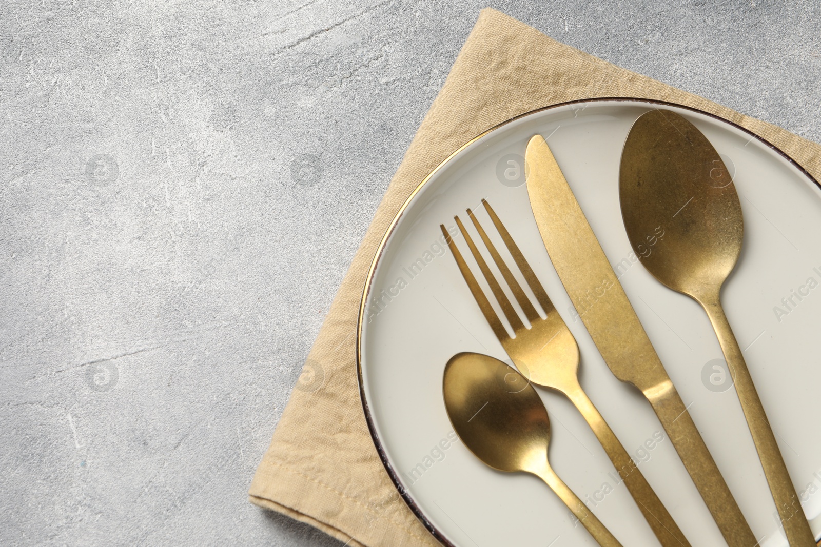 Photo of Stylish cutlery, plate and napkin on light grey table, top view. Space for text