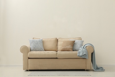 Photo of Comfortable sofa near beige wall in living room interior. Space for text