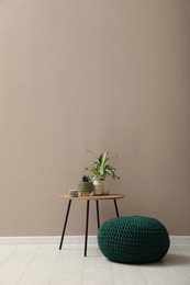 Photo of Knitted pouf and table with houseplants near beige wall indoors. Space for text