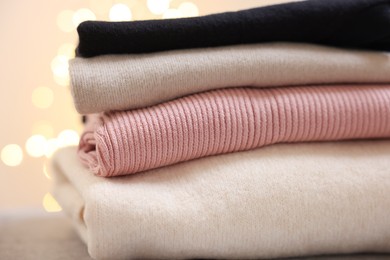 Photo of Stack of folded clothes on grey table against blurred lights, closeup