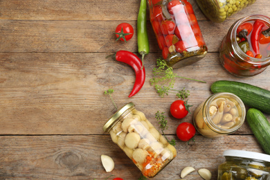 Jars of pickled vegetables and ingredients on wooden table, flat lay. Space for text